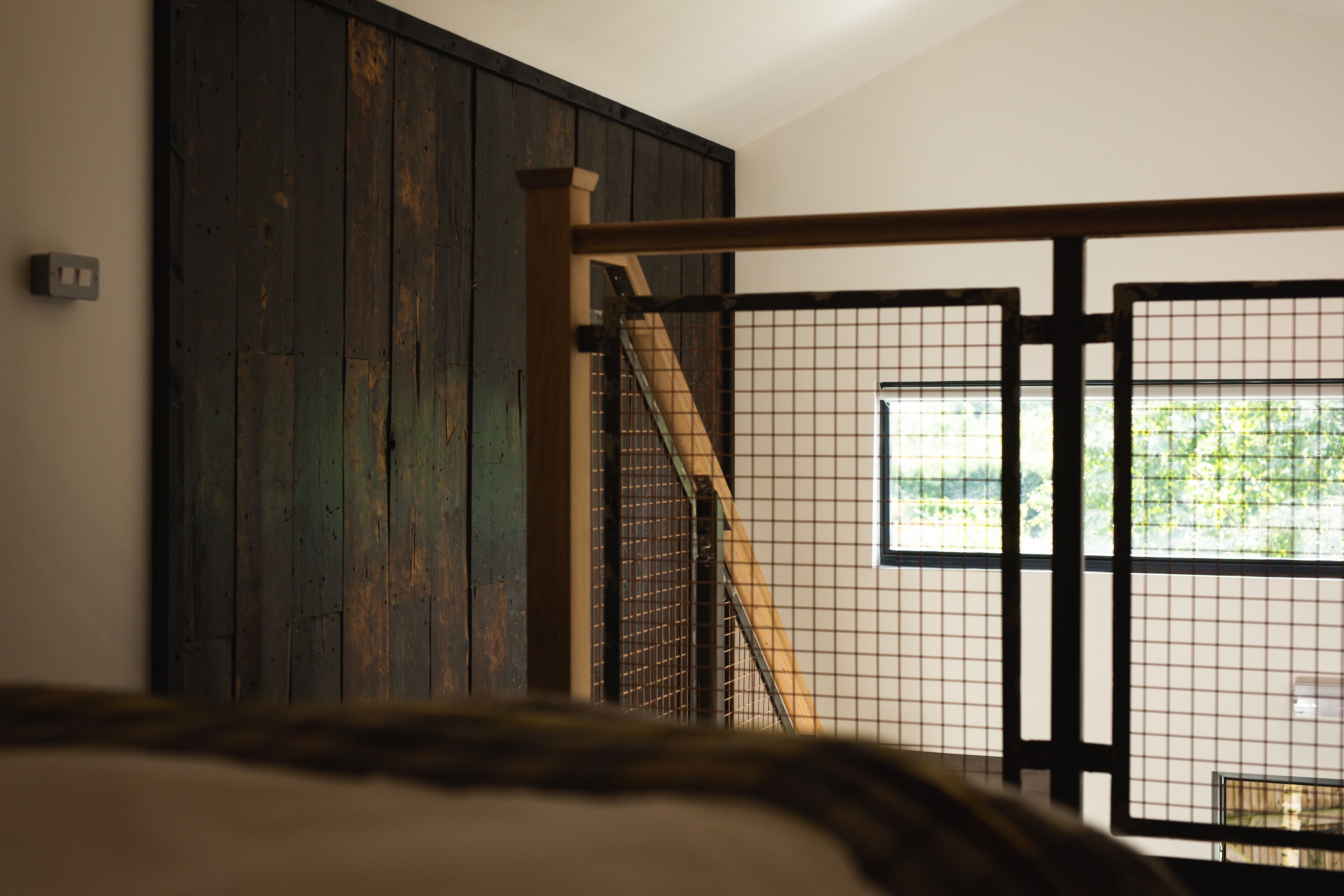 Una escalera con barandilla de madera y metal que conduce a una habitación con un ventanal grande.