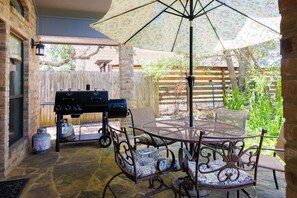 Eine Terrasse im Freien mit Grill, Tisch und Stühlen sowie Sonnenschirm.