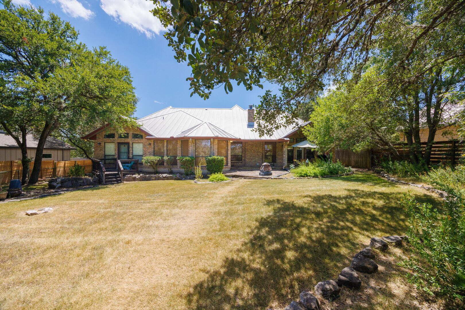 A residential property with a well-maintained lawn, a patio area, and a house with a brick exterior and a metal roof.