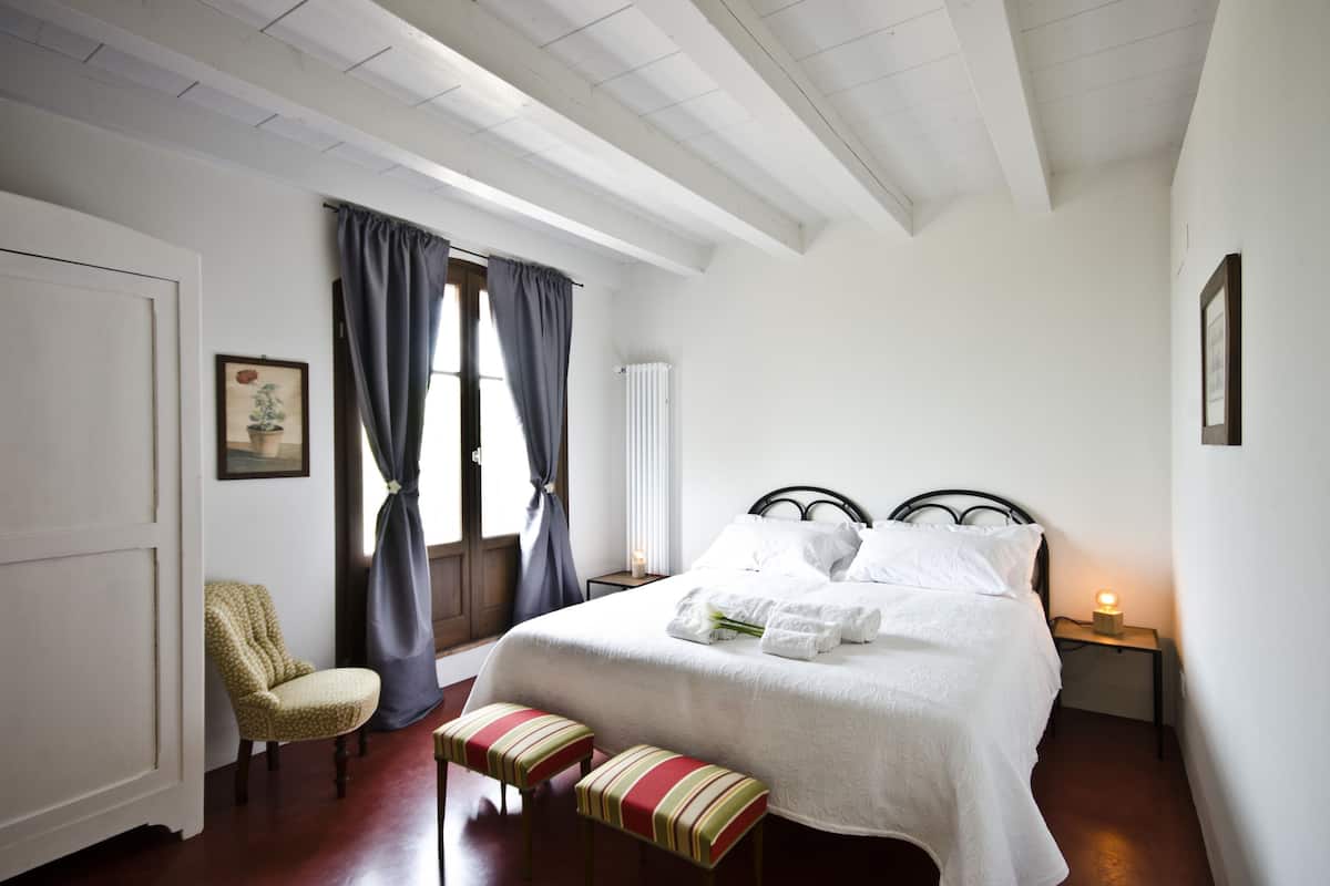 A neatly arranged bedroom with a bed, a chair, a bench, and a bedside table with a lamp.