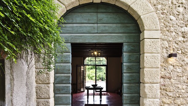 An arched doorway leading into a room with a wooden bench and a table, set against a stone wall with a window above. - Relais Villa Ambrosetti (Verona)