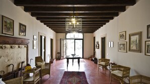 A spacious room with a high ceiling, wooden beams, wicker furniture, and a large window providing natural light. - Relais Villa Ambrosetti (Verona)