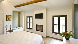 A bedroom with a bed, a chair, a window with a view, a fireplace, and a television mounted on the wall. - Relais Villa Ambrosetti (Verona)