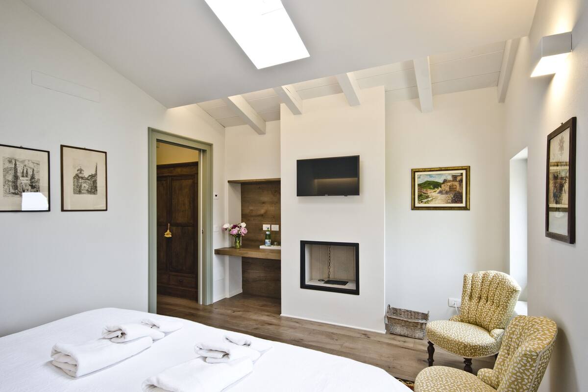 A hotel room with a bed, a chair, a fireplace, and artwork on the walls.