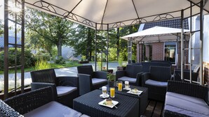 An outdoor patio with wicker furniture, umbrellas, and a view of a garden. - Krasicki Hotel Resort & SPA (Swieradow-Zdroj)