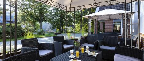 An outdoor patio with wicker furniture, umbrellas, and a view of a garden.