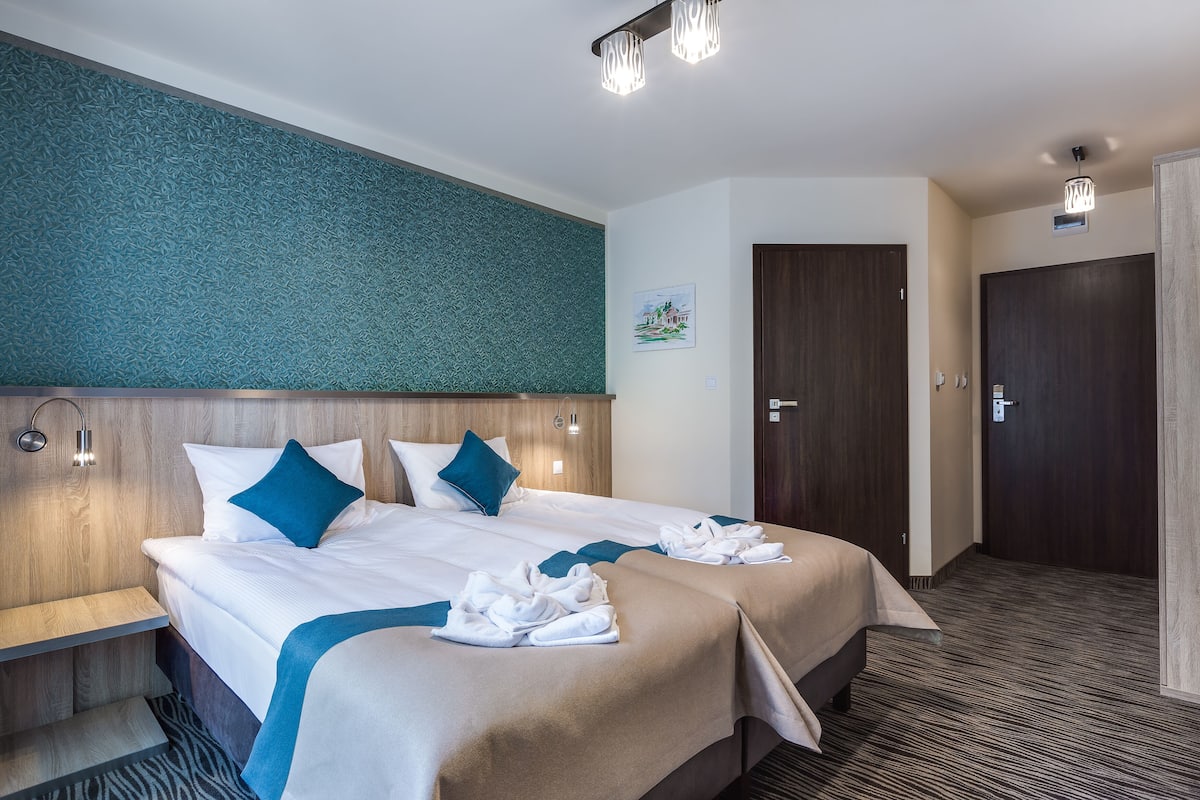 A hotel room with two beds, a wooden headboard, a teal accent wall, and a door to the right.