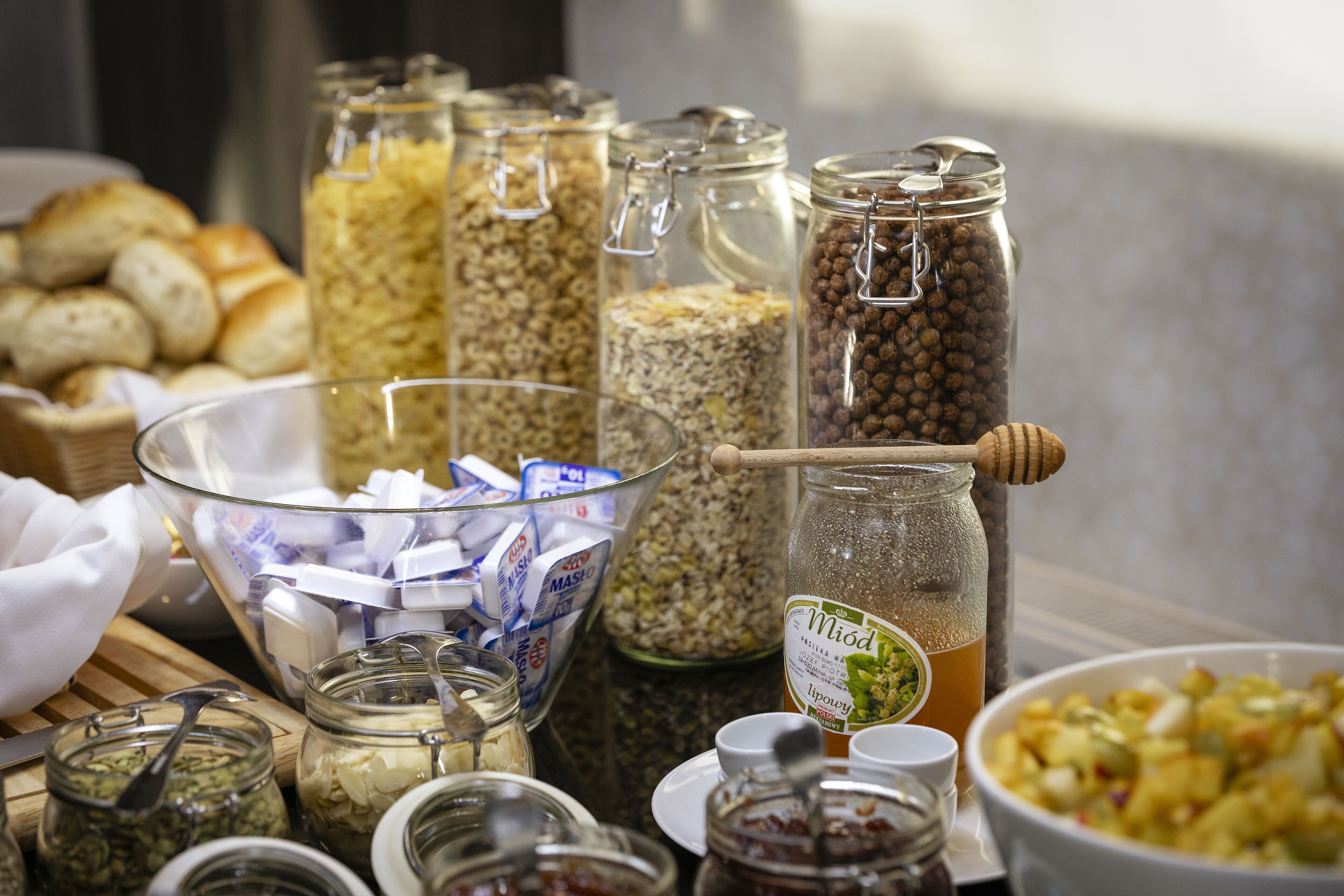 A variety of food items in jars and bowls, including cereals, nuts, and a honey dipper.
