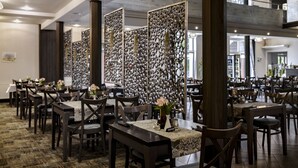 A restaurant with multiple tables and chairs, a decorative partition with circular mirrors, and a carpeted floor. - Krasicki Hotel Resort & SPA (Swieradow-Zdroj)