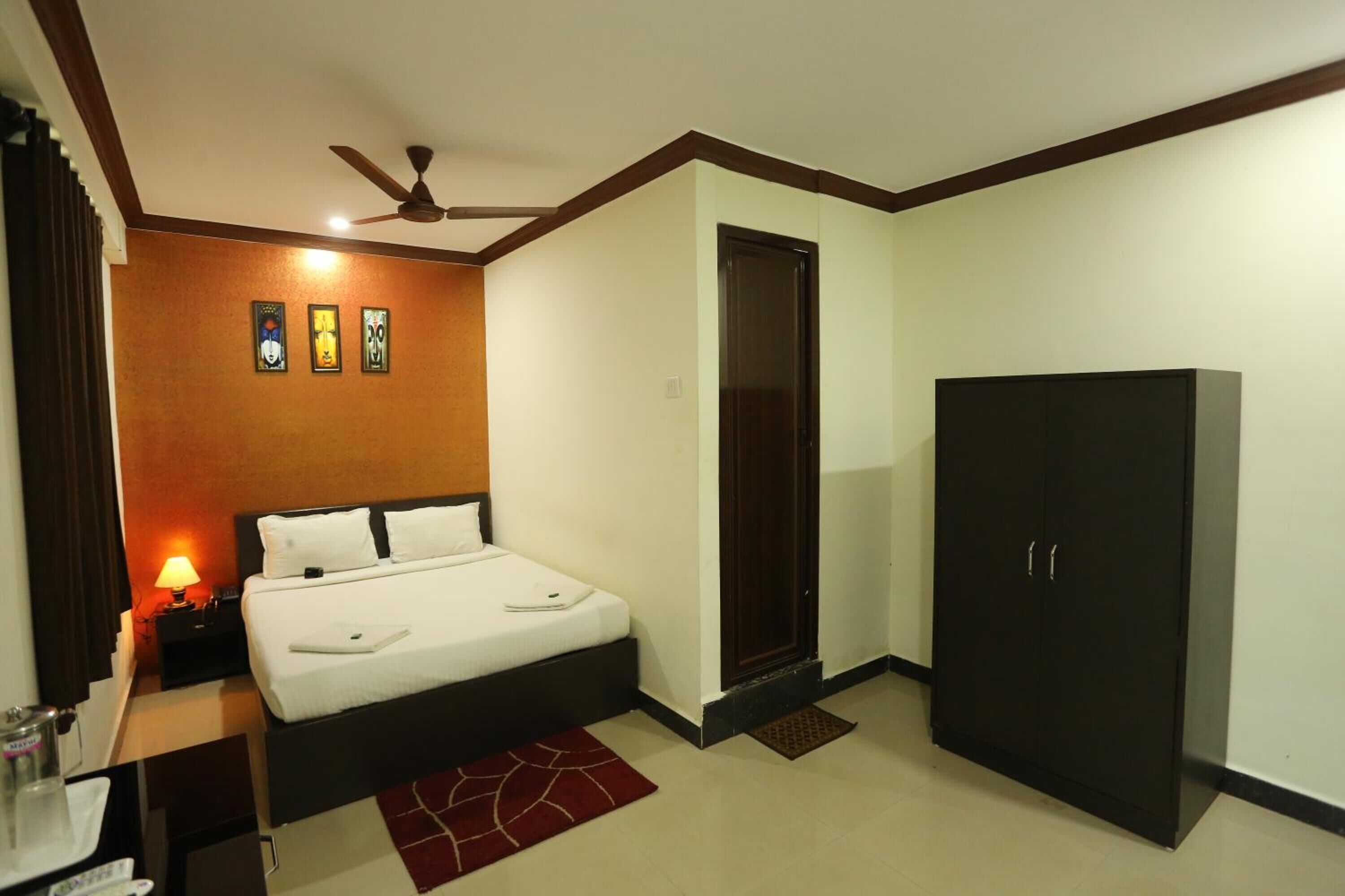 A hotel room with a bed, a wardrobe, a nightstand, a lamp, and a ceiling fan.