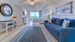 Une chambre moderne avec un lit, un canapé bleu, un bureau et une grande fenêtre.