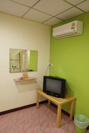 A small room with a television on a wooden table, a mirror on the wall, and an air conditioner mounted above.