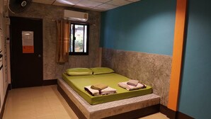 A small, single-bed room with a green mattress, a window with curtains, a ceiling fan, and an air conditioning unit. - White Square Rayong (Rayong)