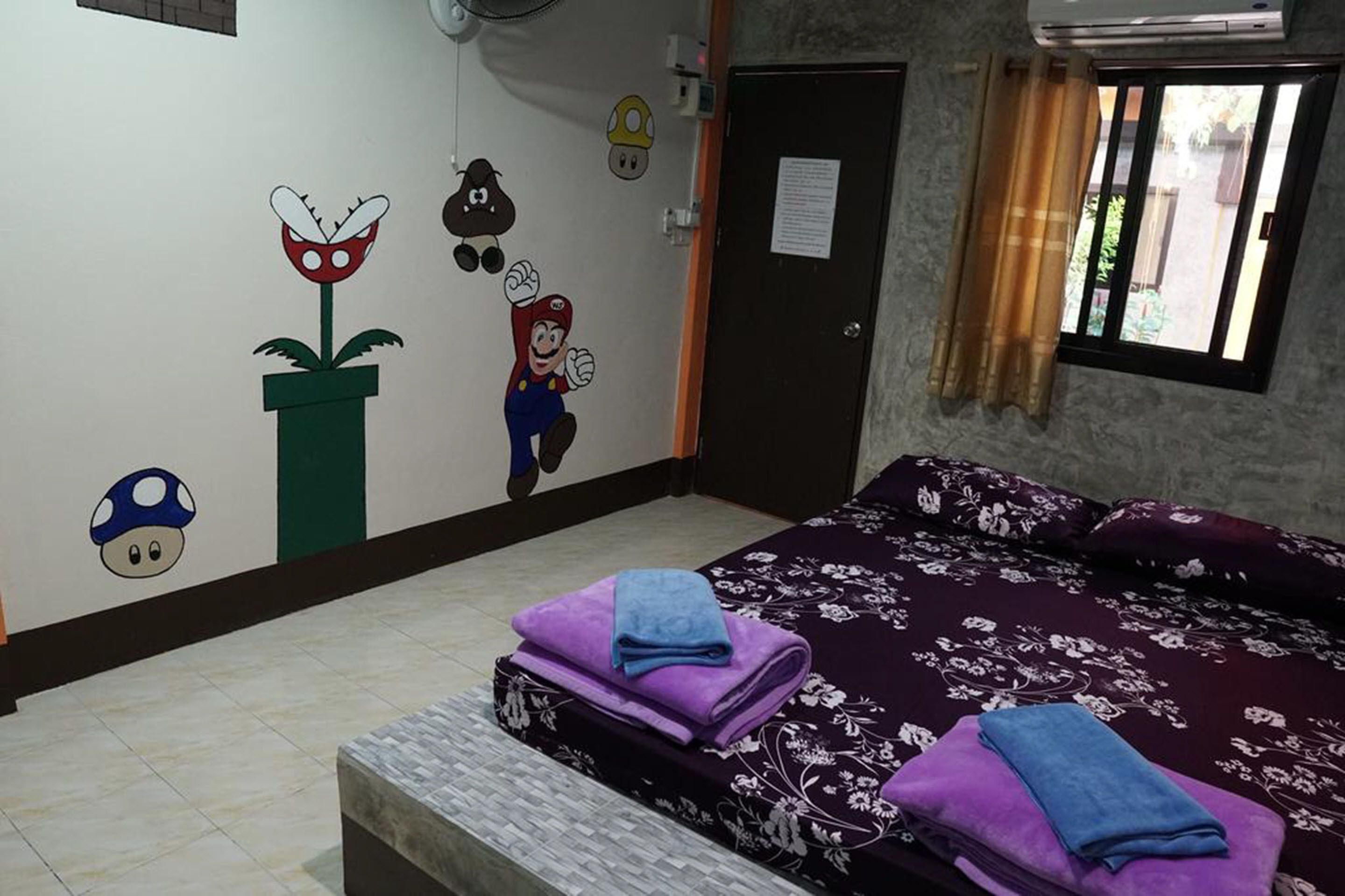 Un dormitorio con cama, pared decorada con personajes de caricatura, puerta y ventana con cortinas.