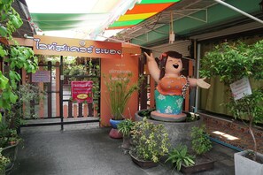 A storefront with a sign in a foreign language, a large statue, and various potted plants. - White Square Rayong (Rayong)