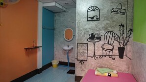 A room with a teal door, a sink, a mirror, a fan, and a wall with a cactus and a bird illustration. - White Square Rayong (Rayong)