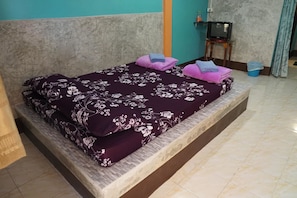 A bed with a floral bedspread, pillows, and a television on a stand.