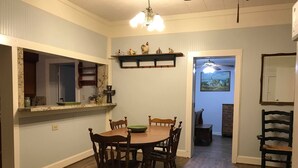 A dining area with a wooden table and chairs, a chandelier, and a kitchen area with a sink and cabinets. - Perfect home in the country (Burton)