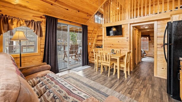 L’intérieur chaleureux d’un chalet, avec un revêtement mural en bois, un coin repas et un téléviseur fixé au mur.