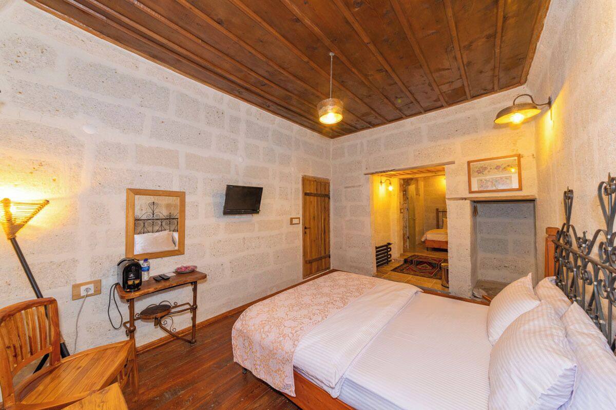 A cozy room with a wooden ceiling, a bed with white linens, a desk with a chair, and a fireplace.