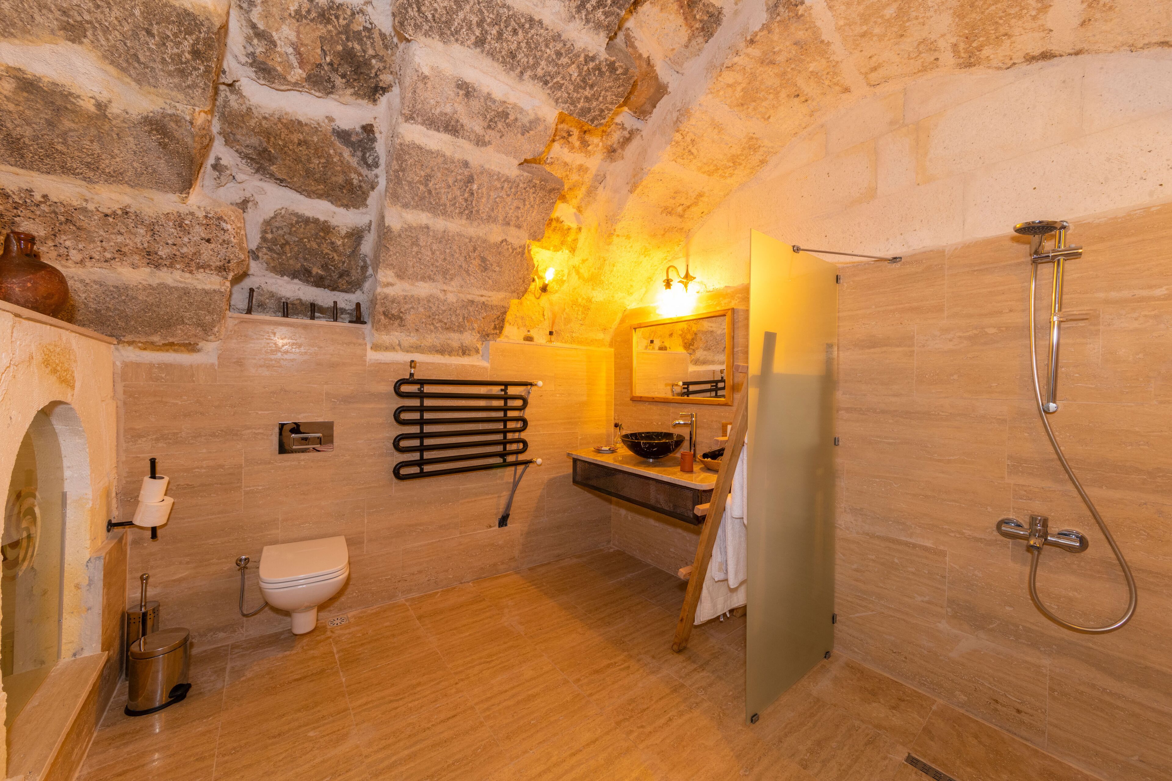 A bathroom with stone walls, a wooden floor, a sink, a toilet, and a shower.