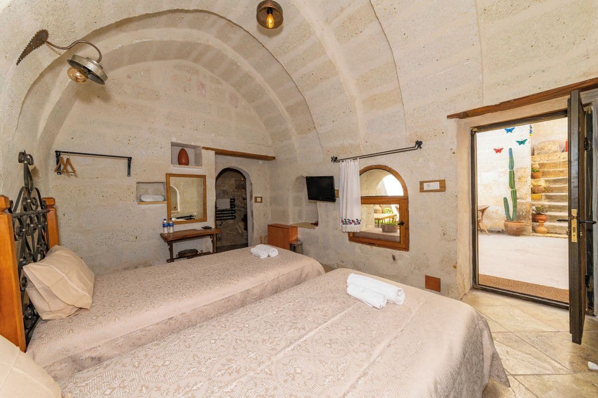 A room with two beds, a mirror, a sink, and a door leading to a balcony with plants.
