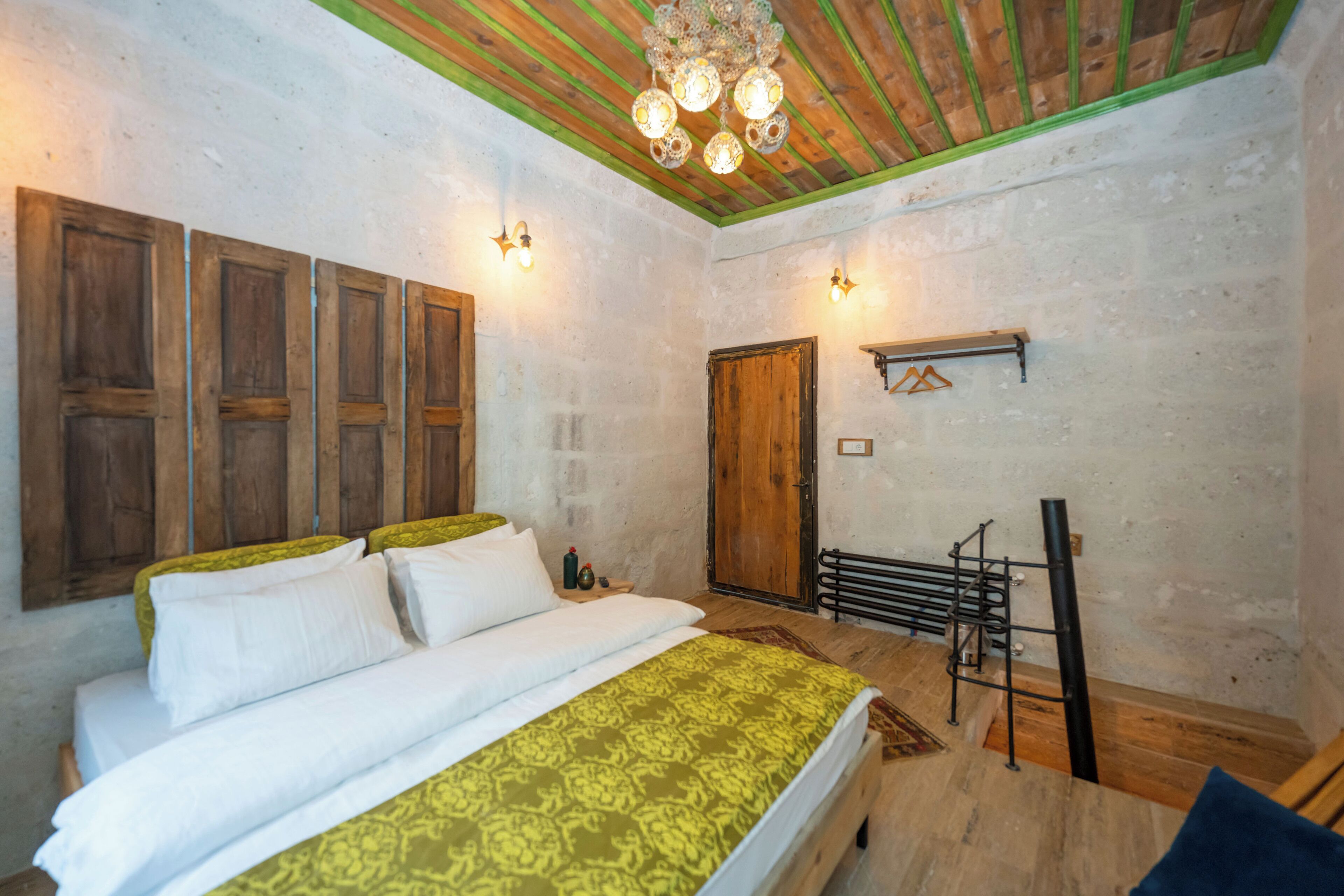 A bedroom with a wooden bed, a green patterned bedspread, a wooden door, and a hanging light fixture.