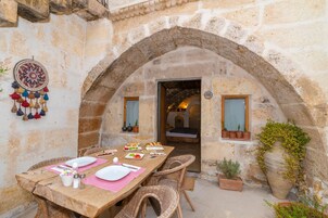 Un espacio de comedor al aire libre con paredes de piedra, una mesa de madera dispuesta para una comida y plantas en macetas.