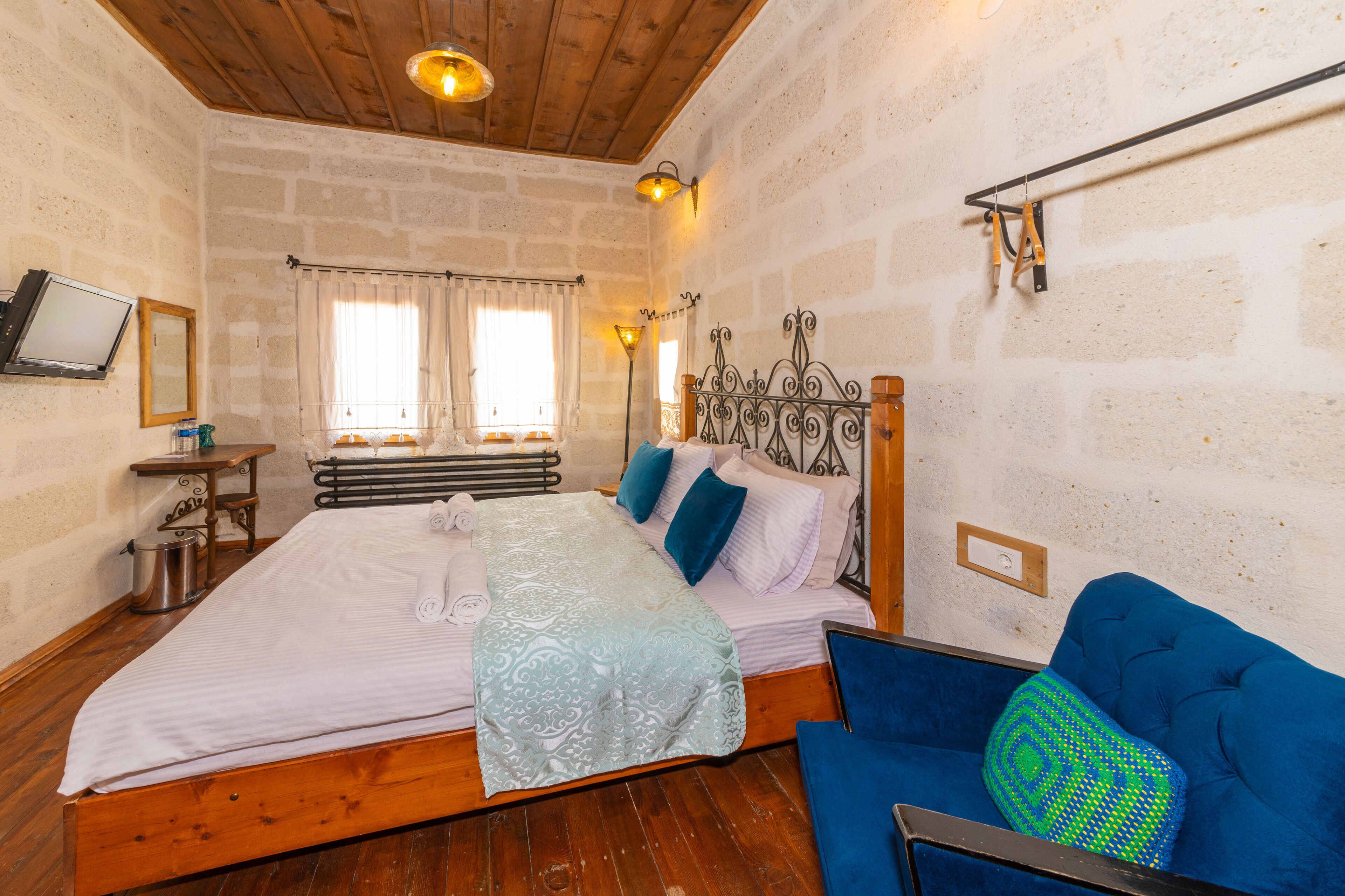 A bedroom with a wooden bed, a blue sofa, and a stone wall.