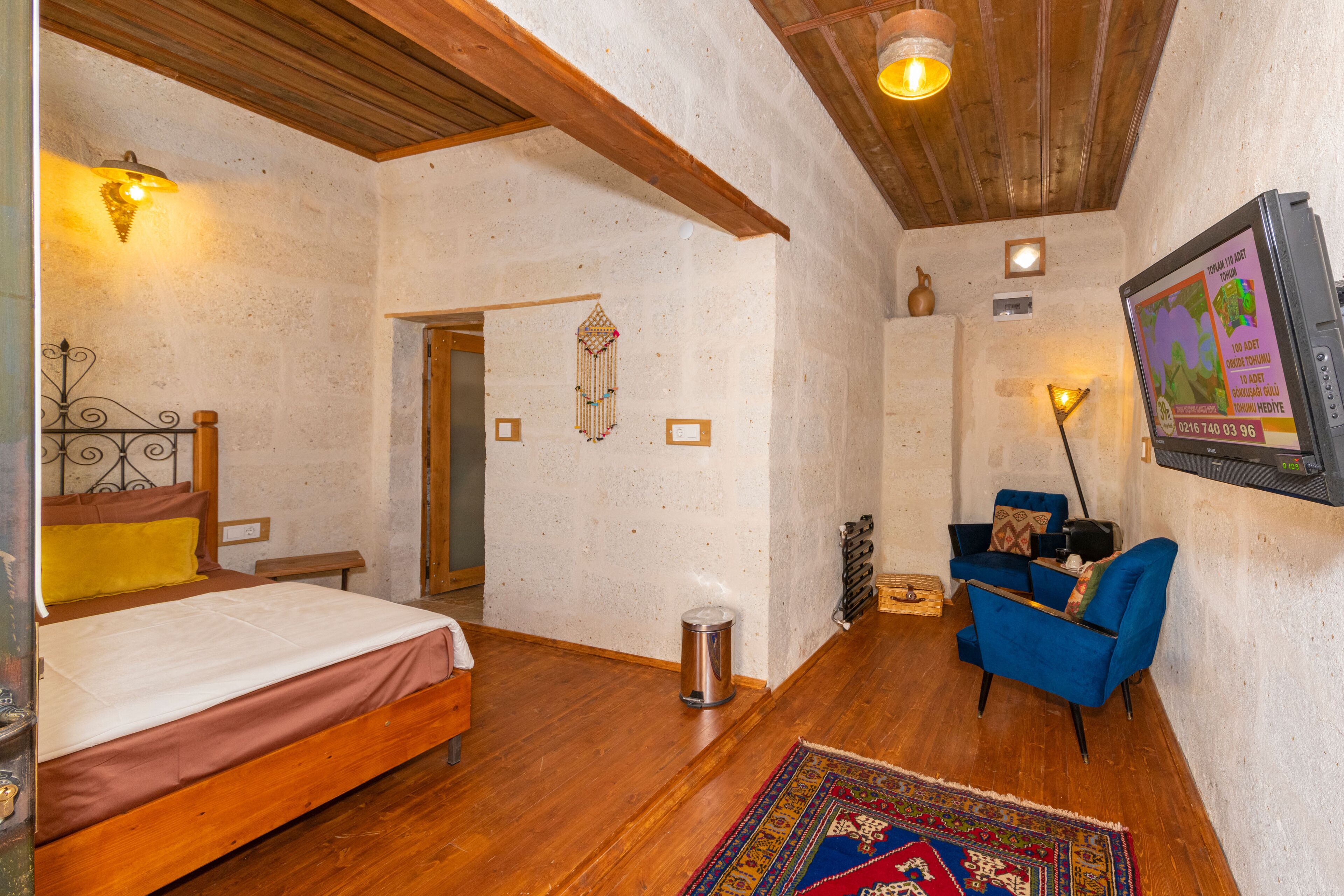 A bedroom with a wooden bed, a blue armchair, a rug, and a wall-mounted TV.
