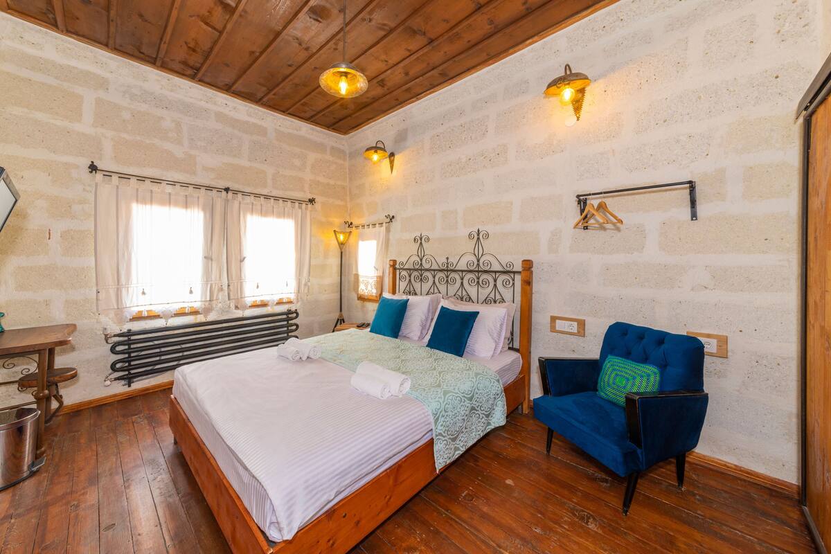 A bedroom with a wooden bed, a blue armchair, a radiator, and a stone wall.
