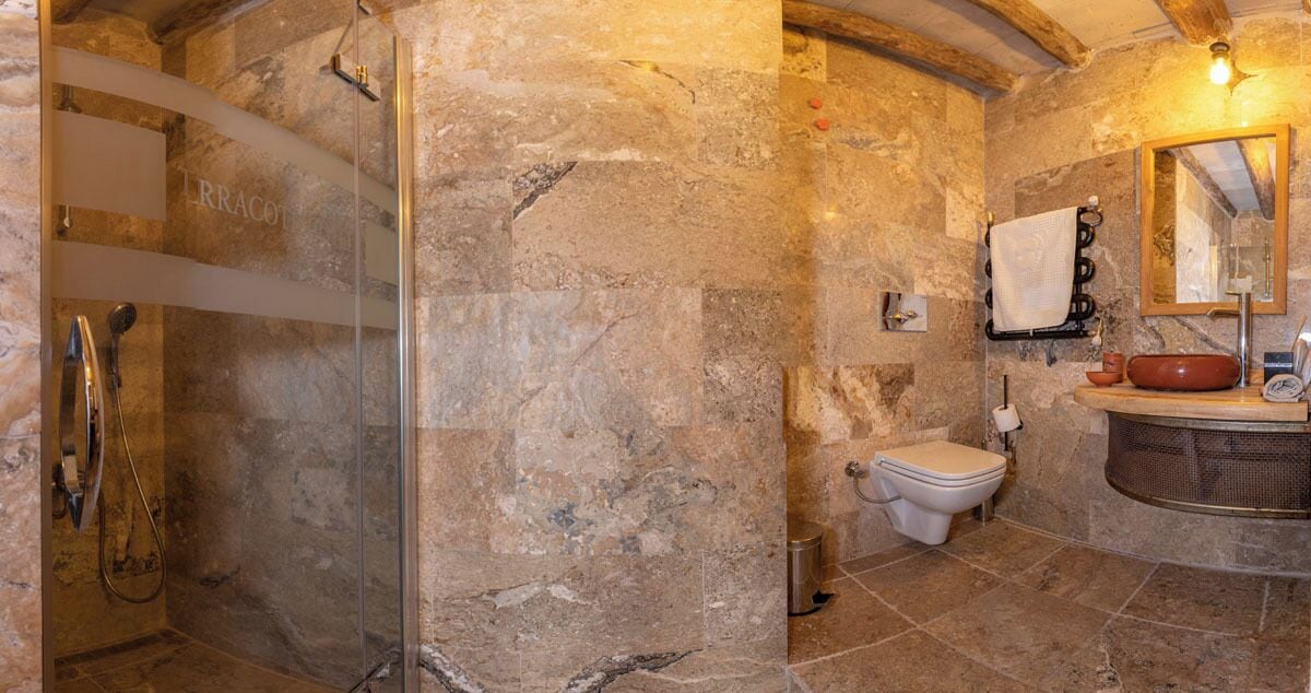 Un baño con paredes de piedra, cabina de ducha de vidrio, inodoro y lavamanos con espejo.