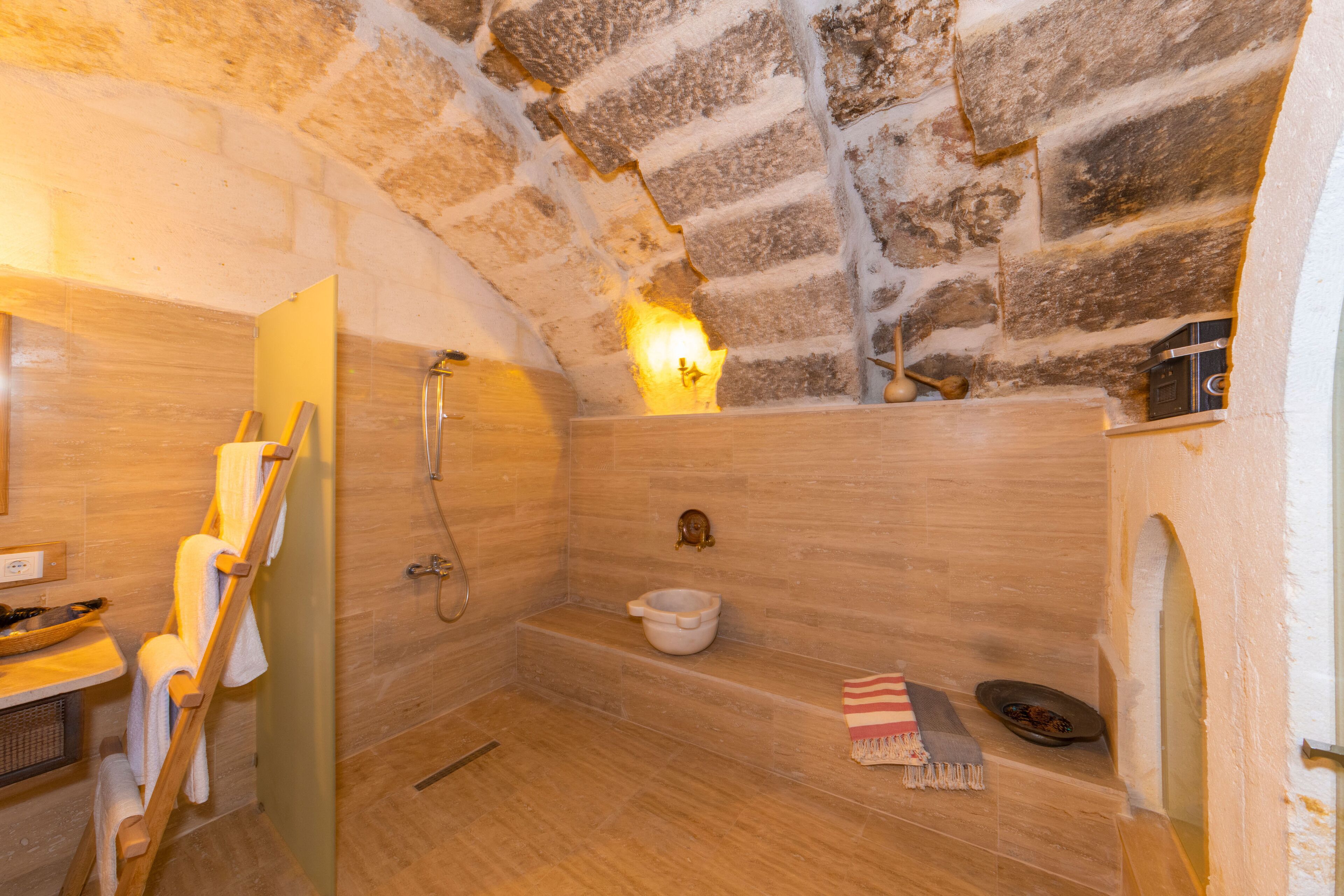 Une salle de bain avec un mur en pierre, un plancher en bois, une baignoire, une douche et un porte-serviettes.