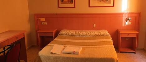 A hotel room with a bed, two nightstands, a desk, and two framed pictures on the wall.
