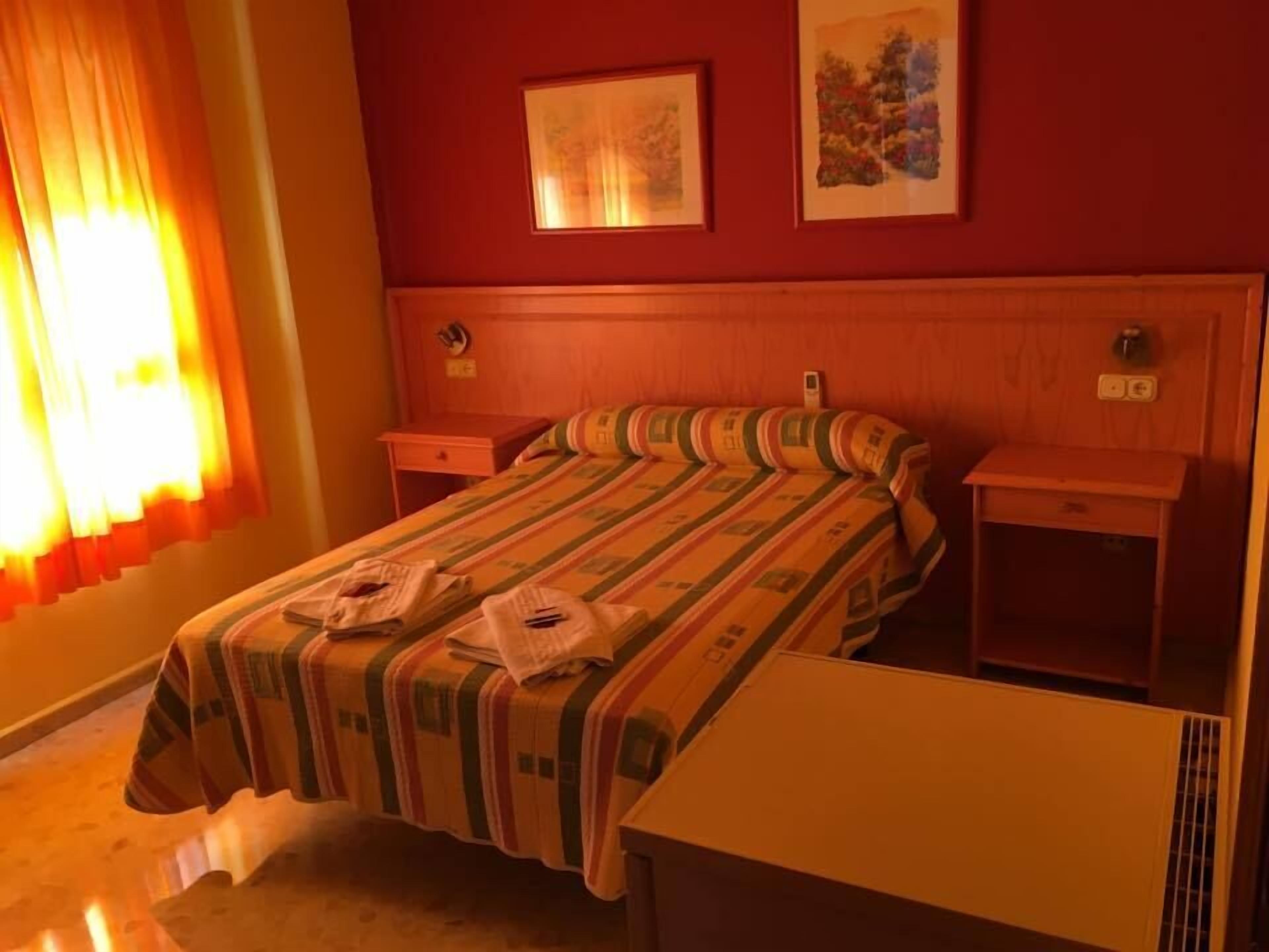 A hotel room with a wooden headboard, a bed with striped bedding, two bedside tables, and two framed pictures on the wall.