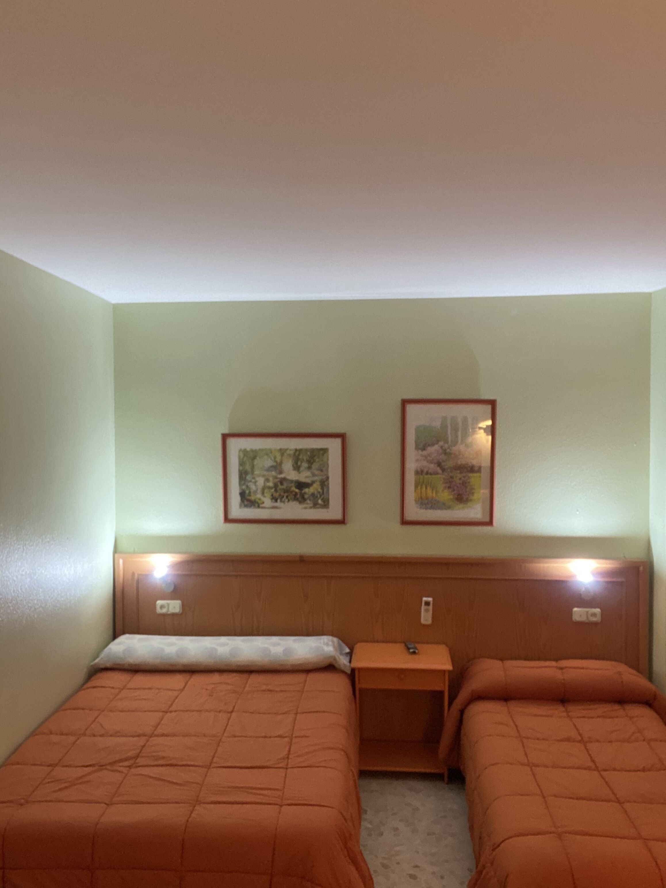 A room with two beds, a nightstand, and two framed pictures on the wall.