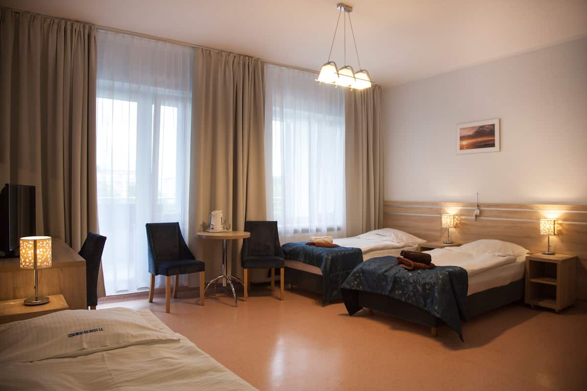 A hotel room with two beds, a desk, a chair, a lamp, and a painting on the wall.