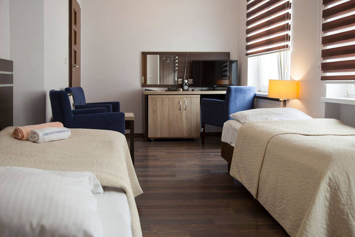 A hotel room with two beds, a desk, a chair, and a TV.