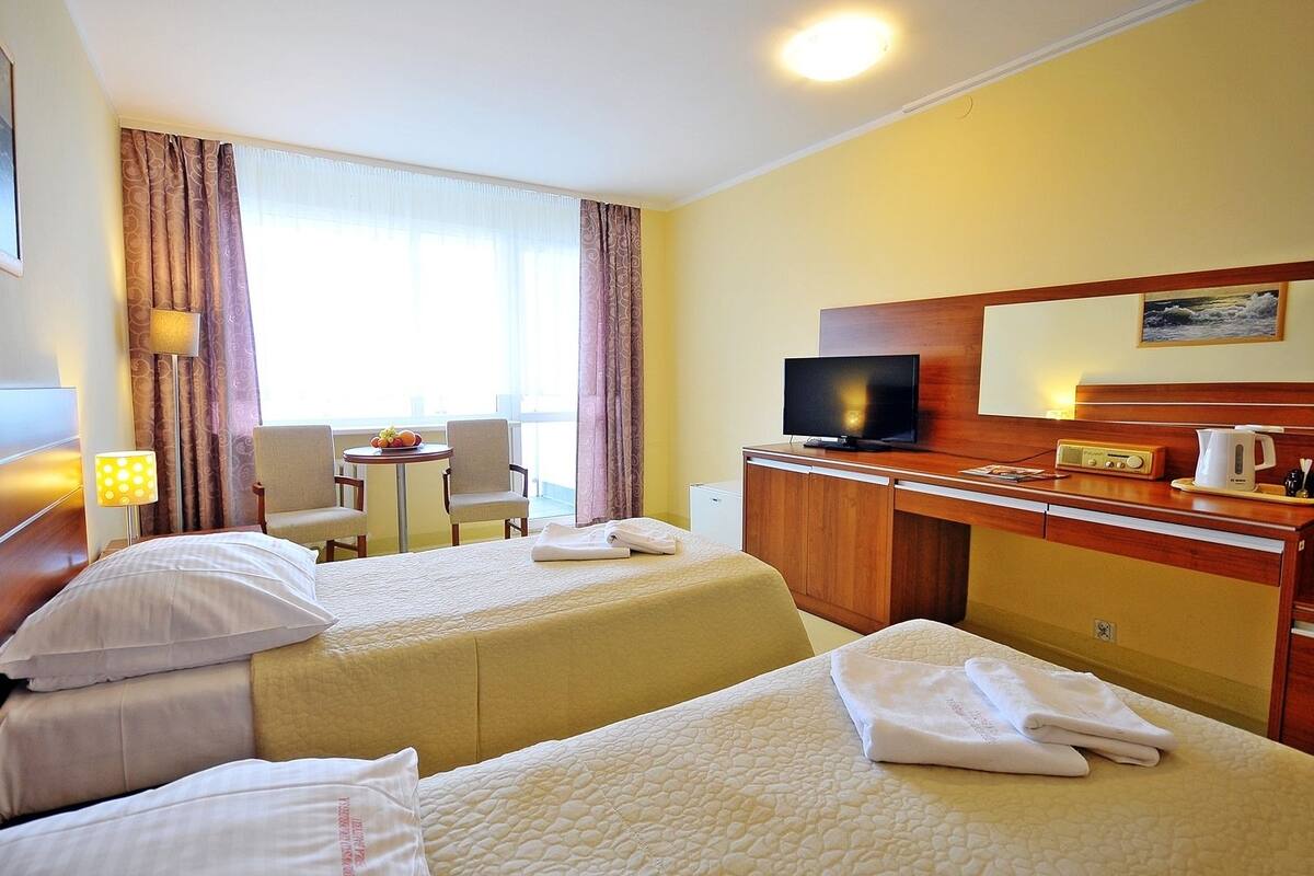 Une chambre d’hôtel avec deux lits, un bureau, une télévision et une petite table avec des fruits.
