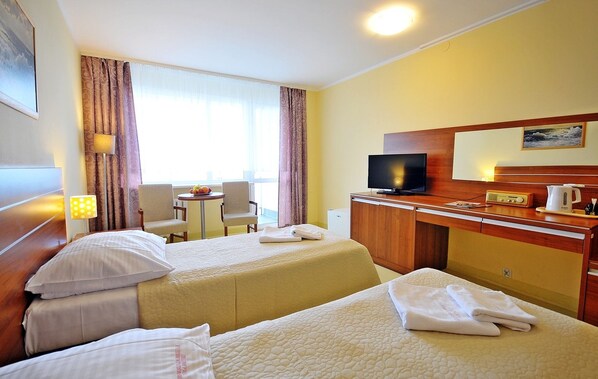 Habitación de hotel con dos camas, un escritorio, un televisor y una mesita con fruta.