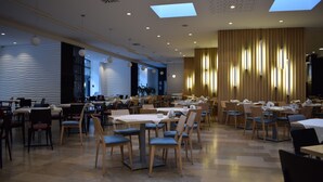 Un vaste espace dédié à la salle à manger, avec de nombreuses tables et chaises, de grandes fenêtres et un plafond moderne agrémenté de lucarnes.