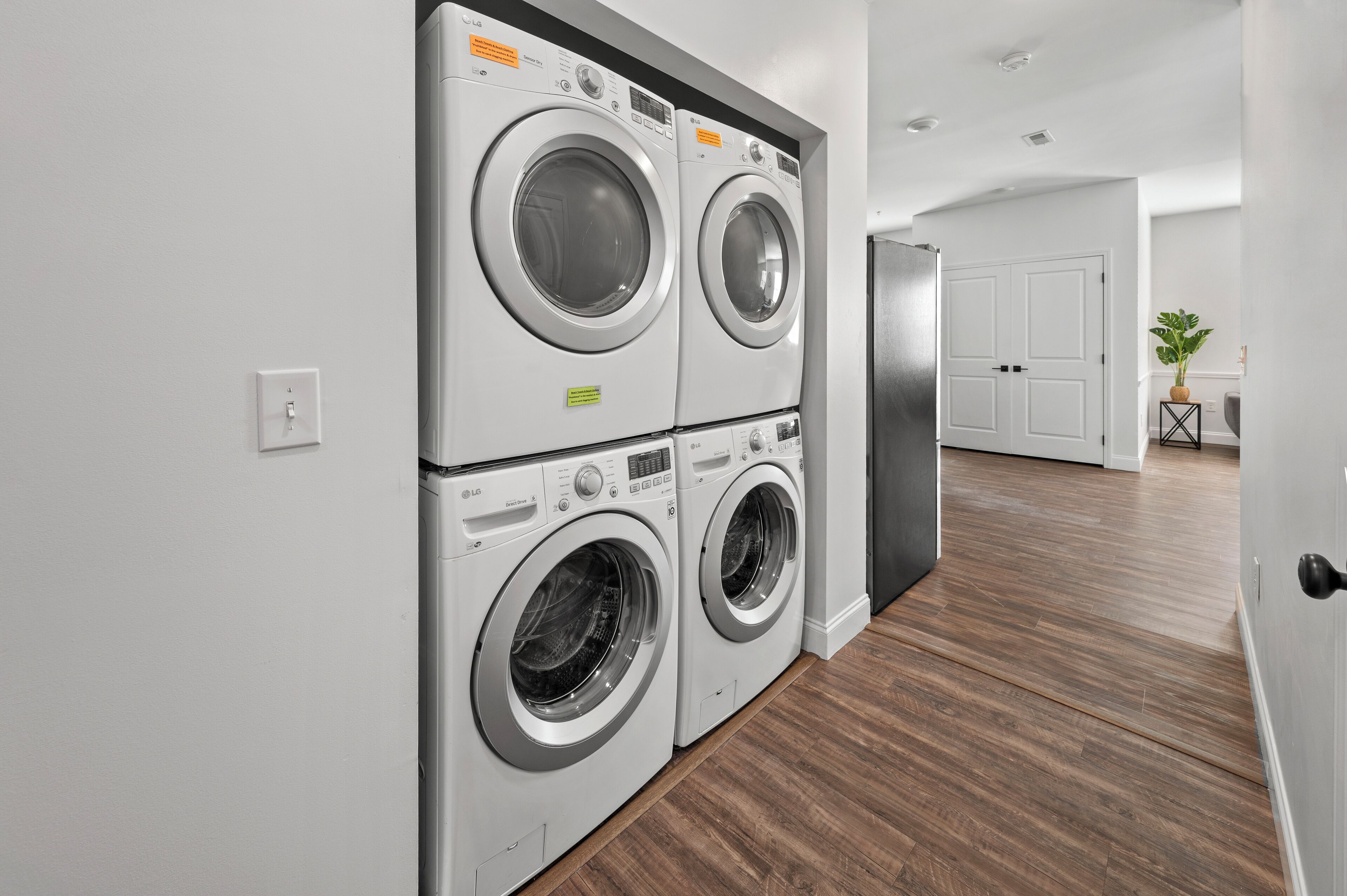 A laundry room with two stacked front-loading washing machines and a stainless steel refrigerator.