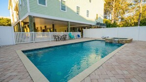 Piscina rectangular con plataforma blanca, rodeada por una cerca blanca y un patio de ladrillo.