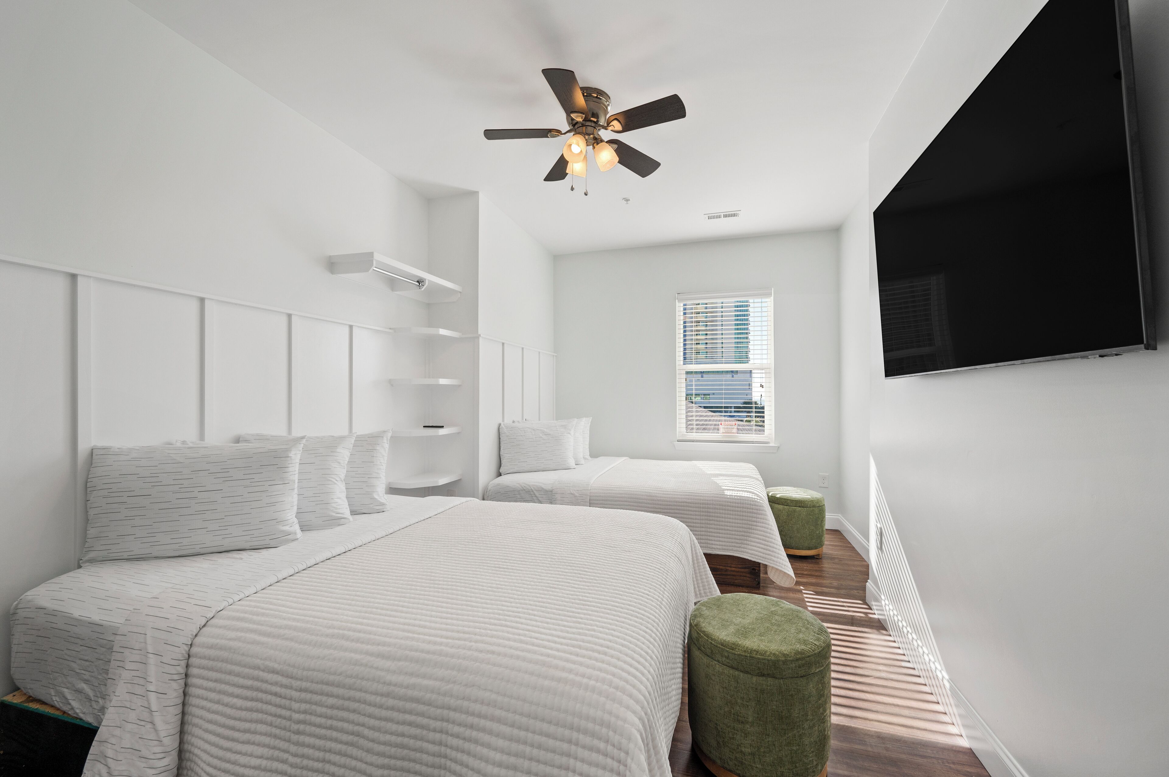 Une chambre moderne avec deux lits, un ventilateur de plafond, une télévision et une fenêtre avec des stores.