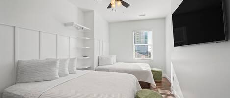 Une chambre moderne avec deux lits, un ventilateur de plafond, une télévision et une fenêtre avec des stores.