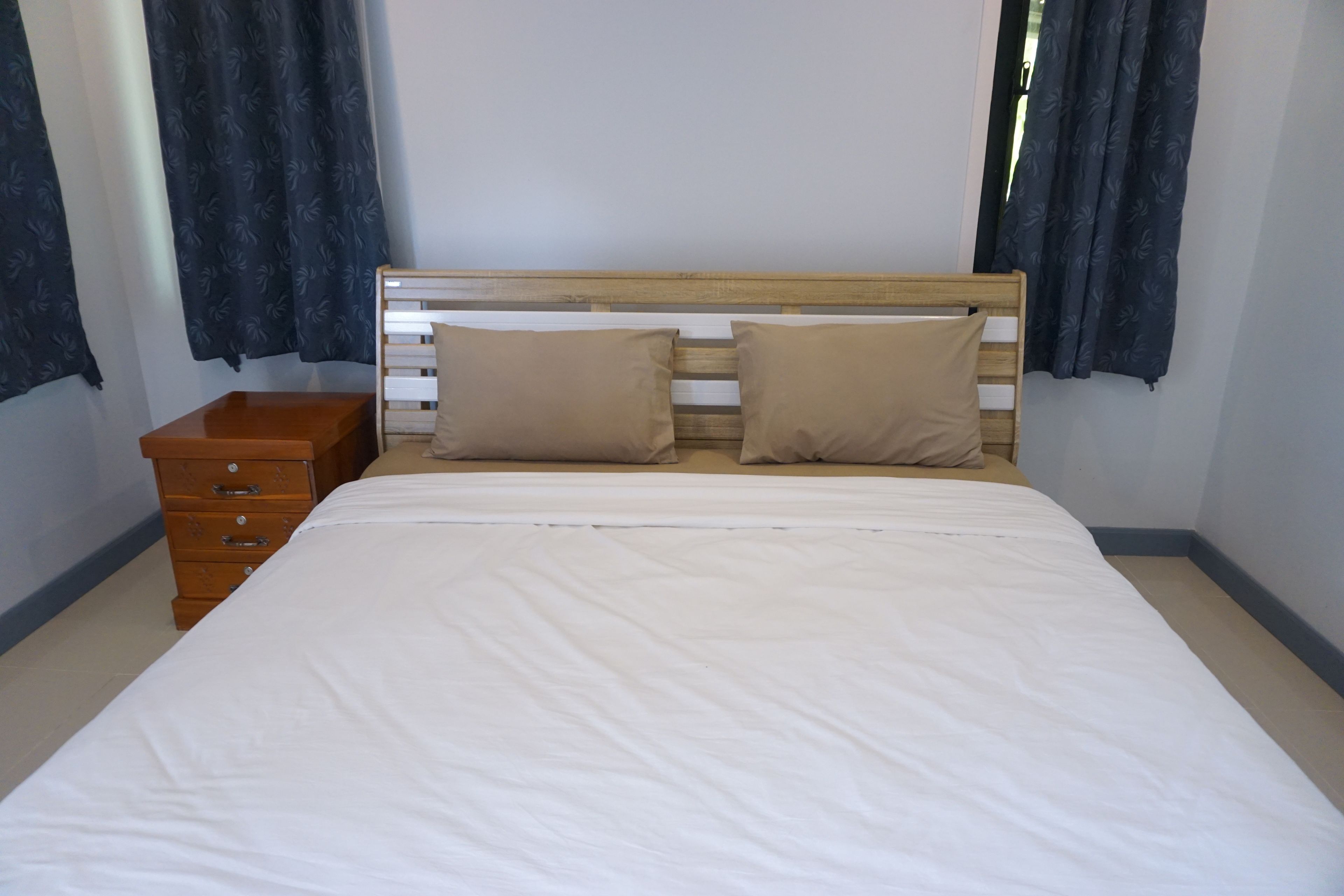 A bedroom with a wooden headboard, two beige pillows, a wooden nightstand, and a white bedspread.