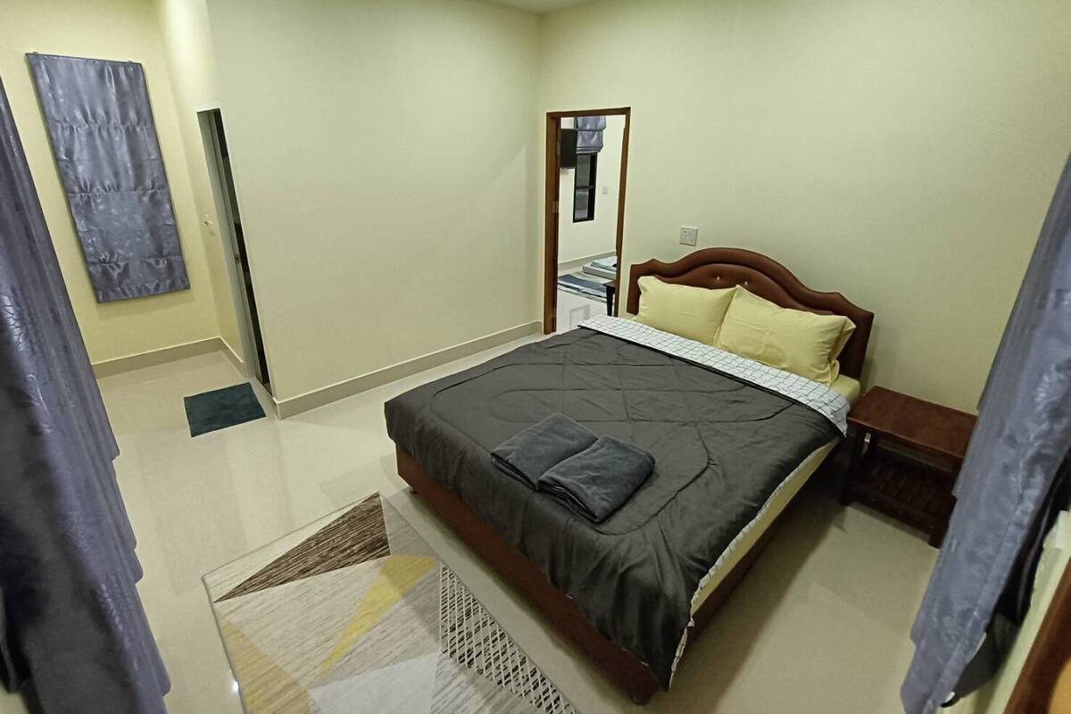 A bedroom with a bed, a nightstand, a mirror, a door, and a small table.