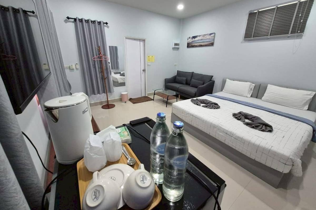 A hotel room with a bed, a sofa, a coffee maker, a kettle, and a tray with bottles and cups.