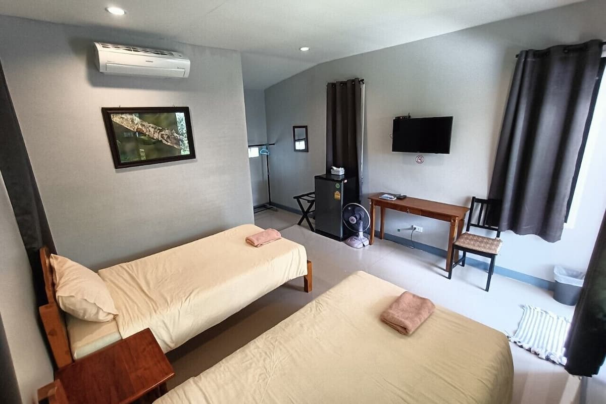 A hotel room with two beds, a desk, a chair, a TV, and an air conditioning unit.