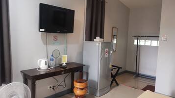 Habitación de hotel con televisión de pantalla plana en la pared, refrigerador, taburete de madera, mesa con tetera, botella de agua y un espejo pequeño.